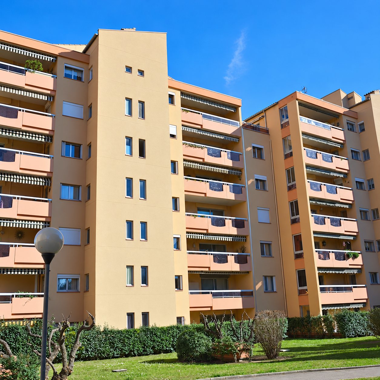 Façade d’un immeuble résidentiel avec balcons et stores sous un ciel bleu