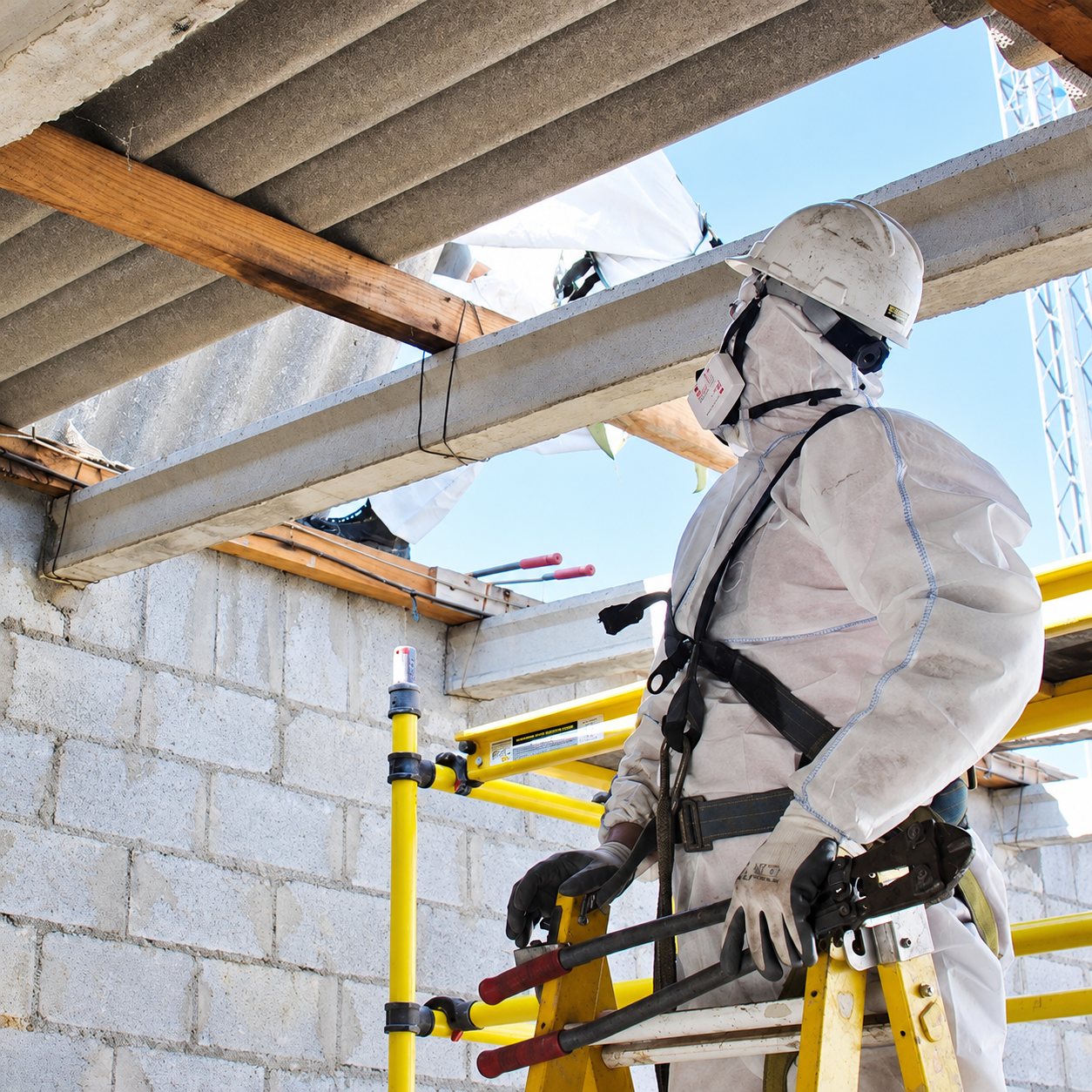 Ouvrier en combinaison de protection sur un échafaudage devant une toiture en fibrociment